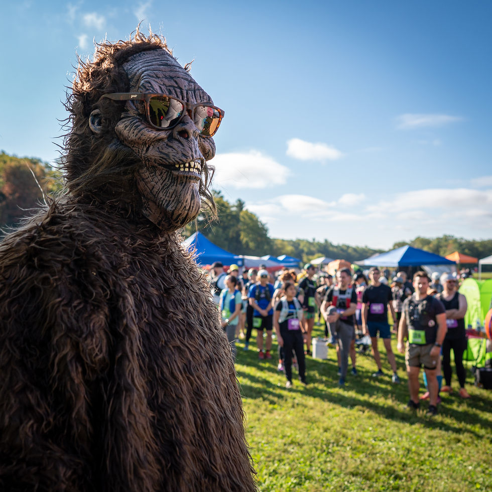 Runner in a Sasquatch costume in front of the start-area crowd at a Sassquad Trail Running trail party