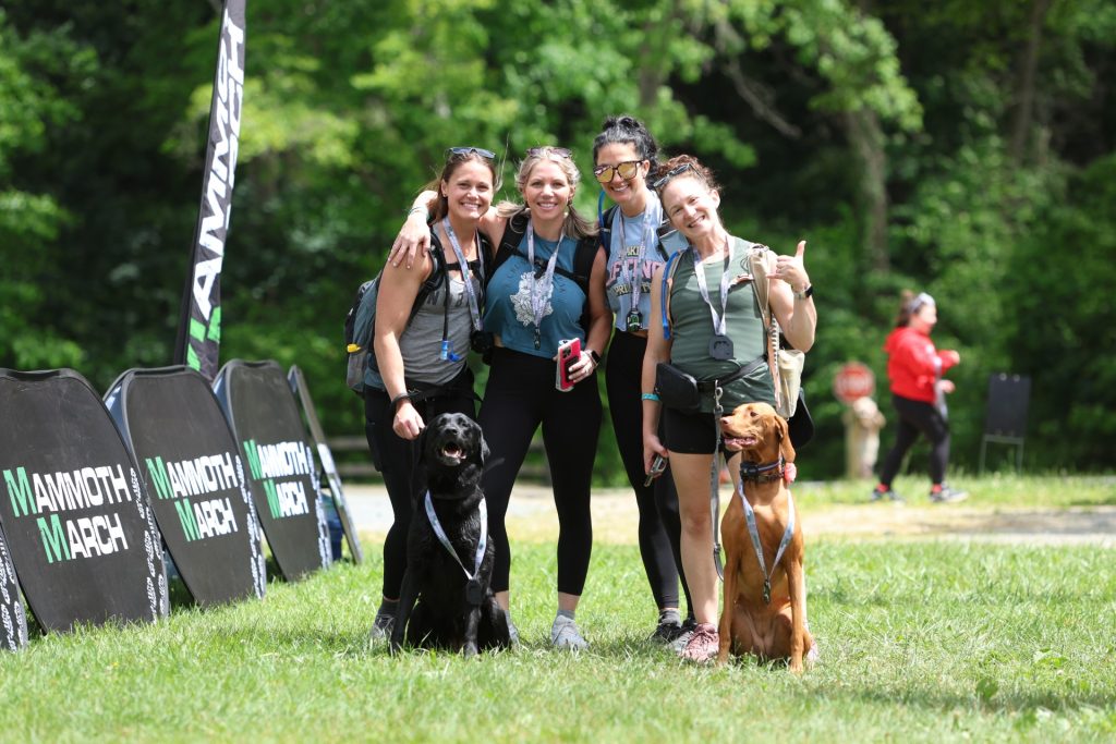 Hikers with backpacks and a dog beside the Mammoth March banners at Delaware Valley