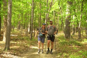 Two Mammoth March hikers with backpacks walking a wooded forest trail