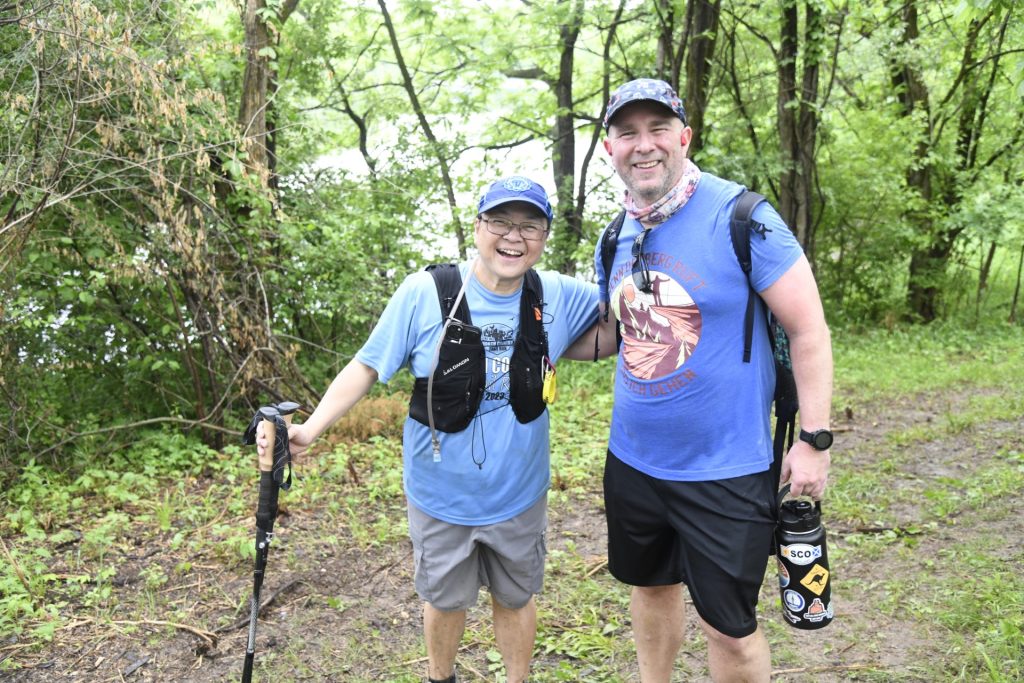 Two hikers with hydration packs and trekking poles on a wooded trail at Mammoth March Illinois