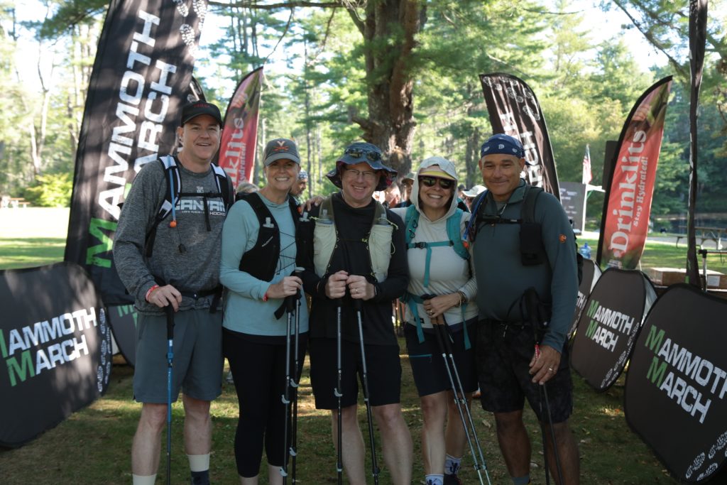A group of hikers with backpacks and trekking poles at the Mammoth March New Hampshire start banners