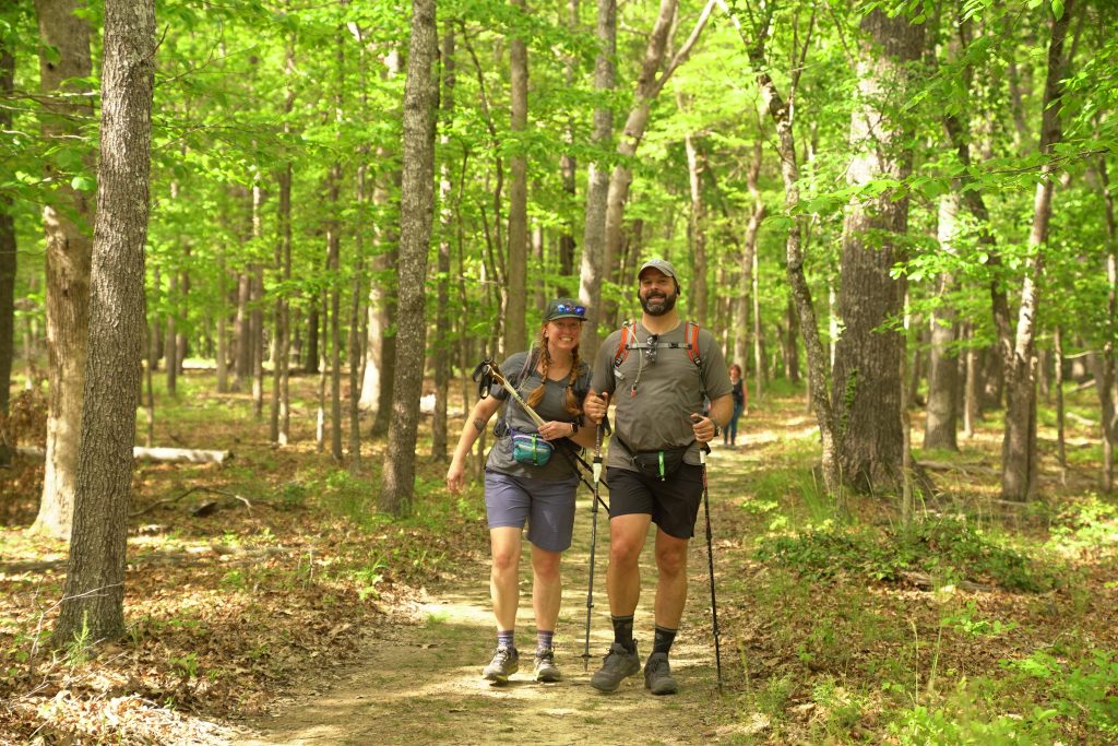 Two Mammoth March hikers with backpacks walking a wooded forest trail