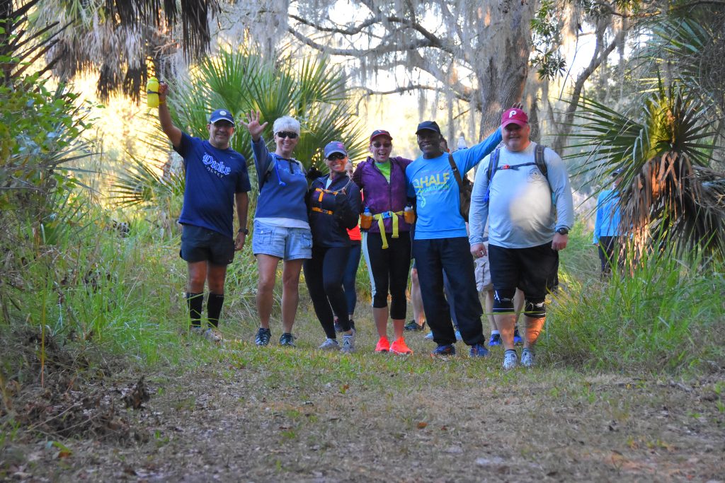 A group of hikers with backpacks on a palmetto-lined trail at Mammoth March Tampa Bay