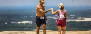 Two racers with trekking poles fist-bumping on the granite slope of Stone Mountain during Stone Everest ATL