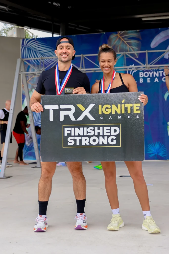 Two TRX Ignite Games finishers with medals in front of the event backdrop