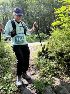 Trail runner with poles climbing a green wooded singletrack at Thunder Chicken