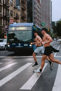 Two Urban Iron athletes running across a Manhattan crosswalk in front of a city bus