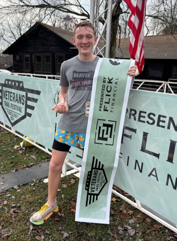 A runner holds the finish tape in front of the Veterans Trail Festival banner at Raccoon Creek State Park