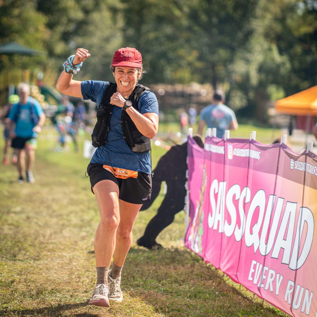Runner passing a Sassquad Trail Running banner in a grass field at Wild Goose Trail Festival