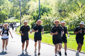 A group of ruckers carrying weighted packs walking toward the camera along a tree-lined path in Central Park during the Blackstone Veterans Network Charity Ruck March
