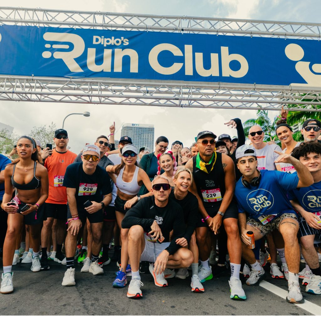 A large group of runners wearing race bibs gathered under the branded Diplo's Run Club start gantry before a 5K