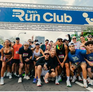 A large group of runners wearing race bibs gathered under the branded Diplo's Run Club start gantry before a 5K