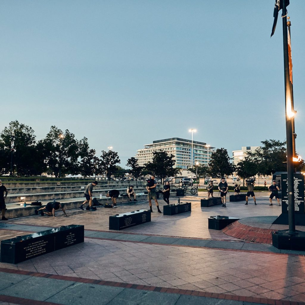 Group of participants performing a rucking challenge together in a public plaza at dusk