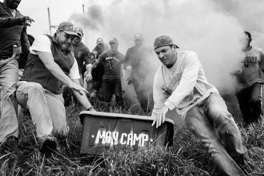 Men hauling a crate stencilled MAN CAMP through smoke during a camp challenge in a field