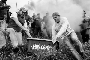 Men hauling a crate stencilled MAN CAMP through smoke during a camp challenge in a field
